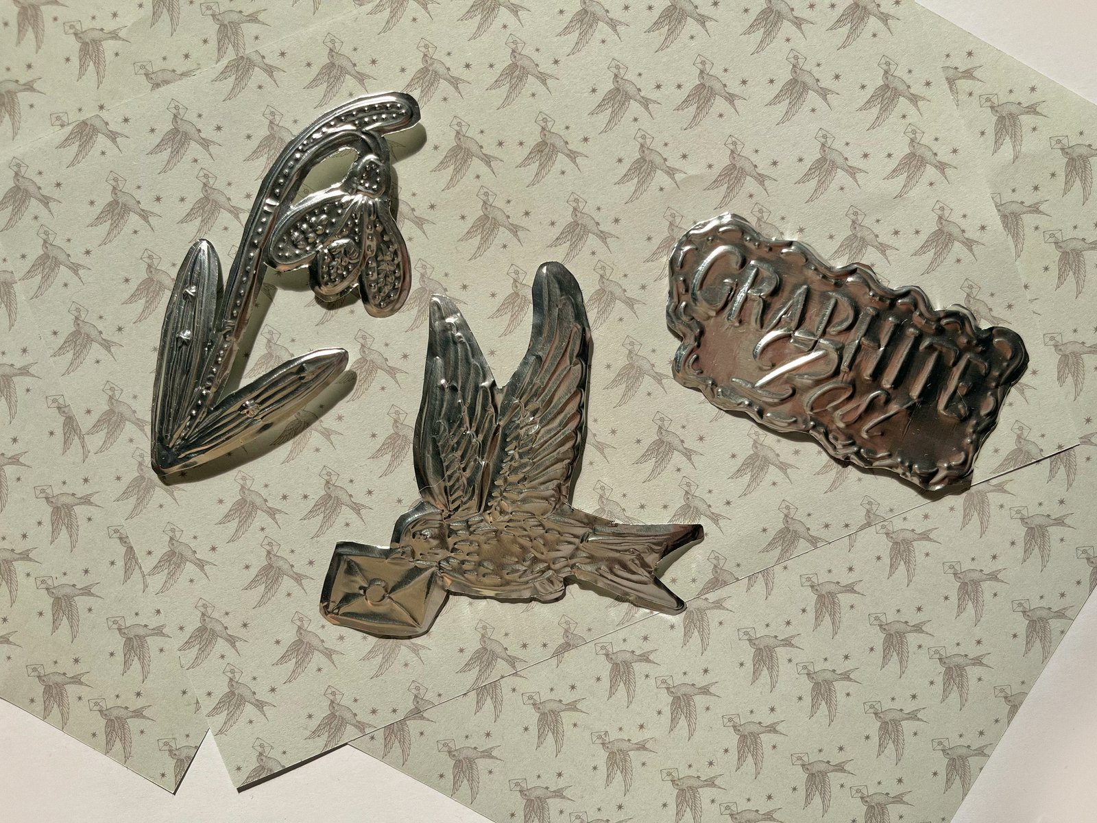 Metallic decorative objects: swallow bird, snowdrop flower, and branded emblem